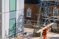 A scaffolder carries a wooden plank on a building site, wearing orange hi-vis protection clothes. Royalty Free Stock Photo