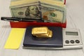 On the scales are three bars of gold, next to it is a pack of dollars. Pen and sheet of paper. Horizontal composition, foreground.