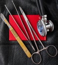 Scalpel tweezers needle holder stethoscope on red document black background leather texture