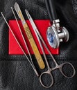 Scalpel tweezers needle holder stethoscope on red document black background leather texture