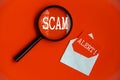 Scam Alert text on magnifying glass and notepad on red cover background. Scamming concept