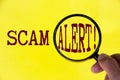 Scam alert text on yellow cover with hand holding magnifying glass. Scamming and fraud concept