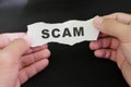 Scammed victim concept. Hand holding a piece of paper with word scam in dark black background.