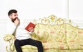 Scandalous bestseller concept. Guy reading book with amazement. Man with beard and mustache sits on baroque style sofa Royalty Free Stock Photo