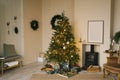 Scandinavian beige Christmas interior with decorated Christmas tree. Fireplace with armchair, mockup frame on the wall and gifts