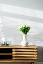 Scandinavian home interior with spring bouquet of white tulip flowers in ceramic vase, tray with candles standing on a