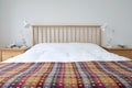 Scandinavian inspired bedroom interior showing wooden bedroom furniture, white painted walls, white bedding and colourful blanket