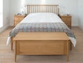 Scandinavian inspired, minimalist bedroom interior showing wooden bedroom furniture, white walls and bedding and grey blanket
