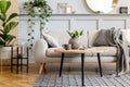 Scandinavian living room interior with design grey sofa, wooden coffee table, tropical plants, shelf, mirror, furniture, plaid. Royalty Free Stock Photo