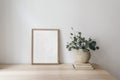 Scandinavian living room interior with poster frame mock up on wooden table, desk. Textured vase with eucalyptus tree