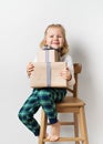 Scandinavian minimalism christmas and new year concept with kid - little girl with stack of gift box on a chair in room, white