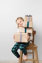 Scandinavian minimalism christmas and new year concept with kid - little girl with stack of gift box on a chair in room, white