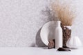 Scandinavian minimalist interior with ceramic vase, dish, dried grass bouquet, brown tree bark, moss in sun beam with shadow.