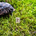 Scandinavian rune Raido, harbinger of travel, on wet moss.