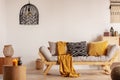 Scandinavian sofa with pillows and dark yellow blanket in bright living room interior with black chandelier