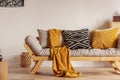 Scandinavian sofa with pillows and dark yellow blanket in bright living room interior with black chandelier