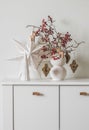 Scandinavian-style Christmas composition on a white chest of drawers - a Christmas bouquet with cranberry branches and paper