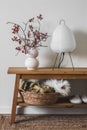 Scandinavian style interior - paper lamp, cranberry branches in a ceramic vase, basket with blankets on an oak bench in the living