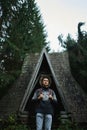 Scandinavian style vertical image man in ethnic sweater and hat standing by old wooden cabin in forest