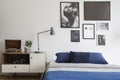 Scandinavian style, wooden dresser by a navy blue bed and framed art gallery on a white wall of a creative bedroom