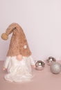 Swedish gnome in white clothes and a beige hat with three silver Christmas balls on a beige background