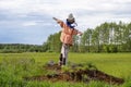 A scarecrow standing in a field wearing an orange jacket, meadow and trees in the background. Royalty Free Stock Photo