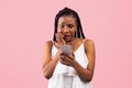 Scared black woman looking at smartphone in terror, seeing bad news, photos or message on pink background Royalty Free Stock Photo