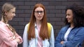 Scared bullying victim looking camera standing near insulting female students