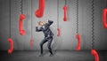 A scared businessman on concrete background hides from many red retro phone receivers hanging down on their cords. Royalty Free Stock Photo