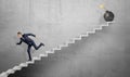 A scared businessman running down grey concrete stairs away from a large iron bomb with a lit fuse. Royalty Free Stock Photo