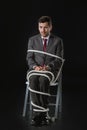 Scared businessman sitting on chair wrapped with ropes