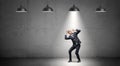 A scared businessman stands cowering under the rays of industrial pendant lights right above him.