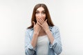 Scared caucasian girl with long chestnut hair, dressed in casual clothes, covering mouth with hands on white background. Keep Royalty Free Stock Photo