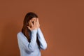 Scared caucasian woman wearing light blue sweater stands sideways to the camera, covers face with hands, is frightened, peeks