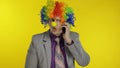 Clown businessman entrepreneur boss talking on mobile phone. Yellow background