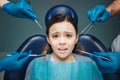 Scared girl sit in detal chair in room. She looks scared and frightened. Adult`s hands in latex gloves hold dentist
