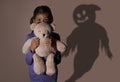 Scared girl with teddy bear suffering from sciophobia and phantom behind her. Irrational fear of shadows