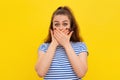 Scared girl in white-blue striped t shirt covers mouth hands and looking at camera with shocked facial expression. Young emotional Royalty Free Stock Photo