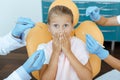 Scared girl with wide open eyes covers mouth with hands and sits in chair