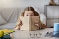 Scared girl with wide open eyes hiding behind a book Royalty Free Stock Photo