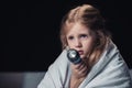 Scared kid sitting under blanket and holding flashlight