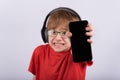 Scared little boy with headphones holding smartphone with blank black screen. Child broke phone. Copy space. Mockup