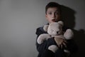 Scared little boy with teddy bear near beige wall. Domestic violence concept