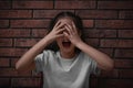 Scared little girl closing eyes with hands near brick wall. Child in danger Royalty Free Stock Photo