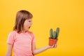 Scared little girl is holding a cactus, isolated on yellow background, Royalty Free Stock Photo