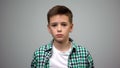 Scared male kid standing grey background, frightened child, orphanage bullying