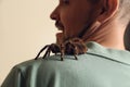 Scared man with tarantula on beige background. Arachnophobia fear of spiders