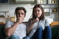 Scared millennial couple watching horror movie on tv at home