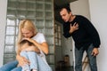 Scared mother and daughter hugging each other sitting on sofa while aggressive standing father angrily yells at them at Royalty Free Stock Photo