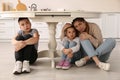 Scared mother with her children hiding under table in kitchen during earthquake